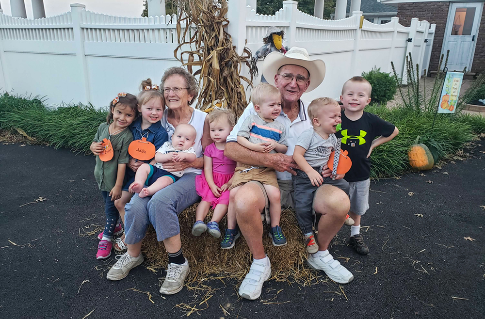 89-year-old Walter Styer sits with his wife, Sarah, on a hay bale, both with their arms wrapped around several young great-grandchildren